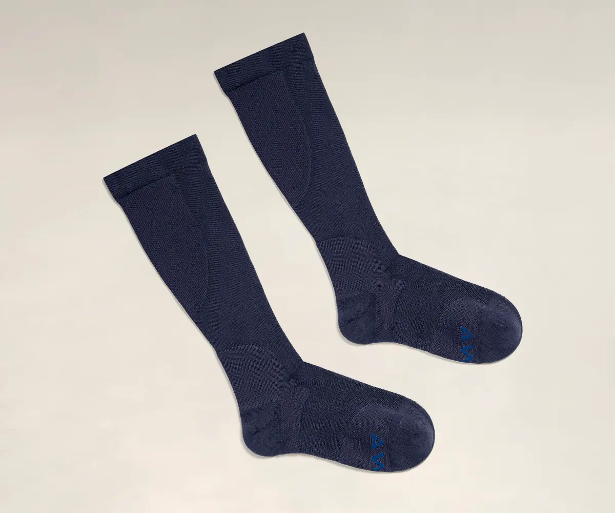 Navy compression socks from Away on a tan background