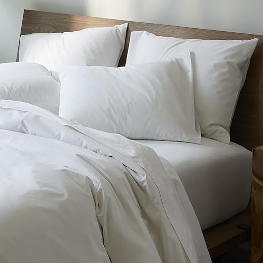 Four pillows on top of a bed covered in white Brooklinen cotton pillowcases