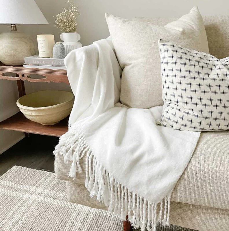 A beige couch with a white Cozy Earth bamboo blanket and throw pillows