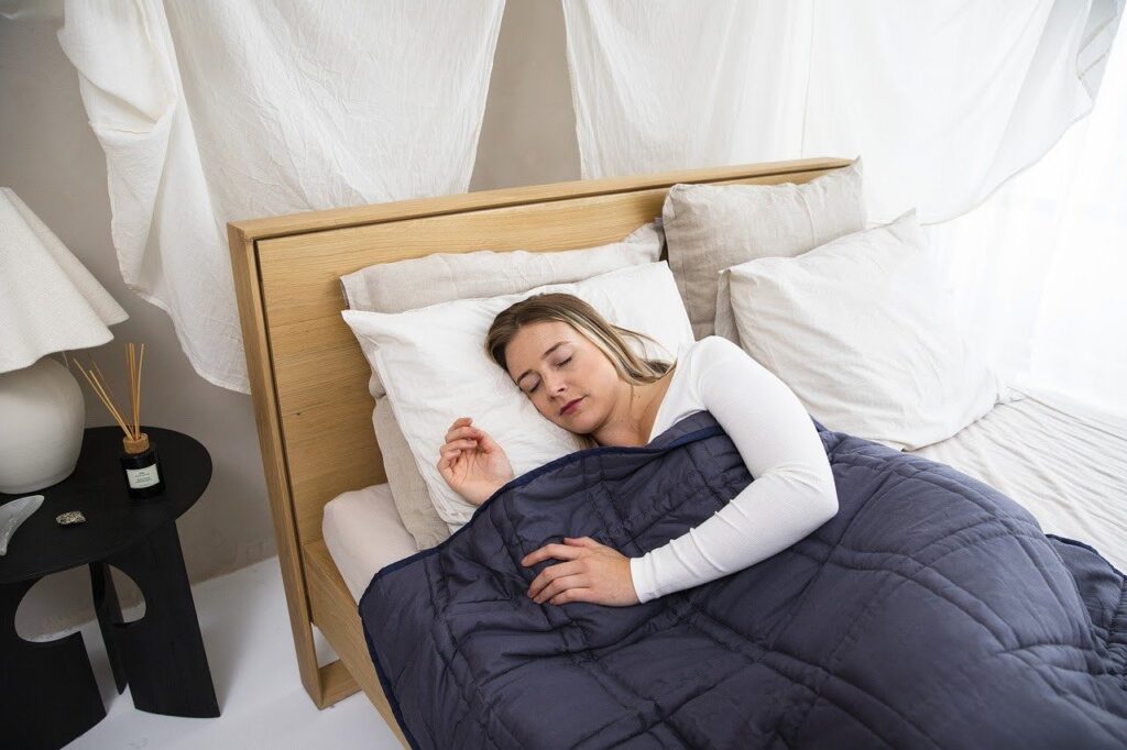 A woman laying in bed sleeping while covered with a thick blue blanket