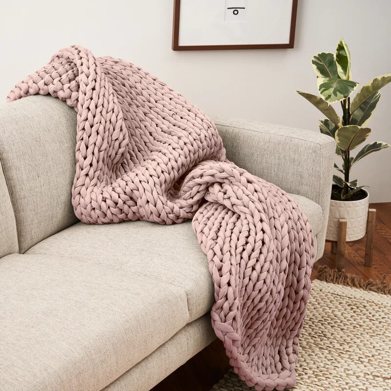 A pink knit blanket draped over a beige couch