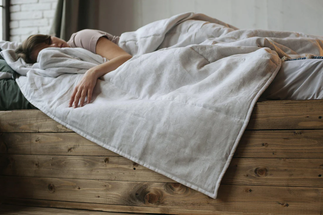 A woman laying on a bed with a white hemp blanket
