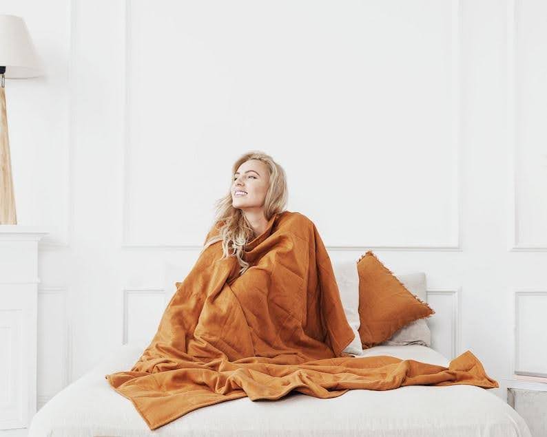 A woman wrapped in an orange linen weighted blanket