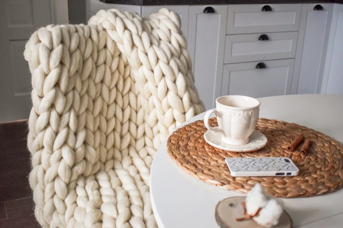 A chunky merino wool blanket draped over the back of a chairl, a table with a teacup