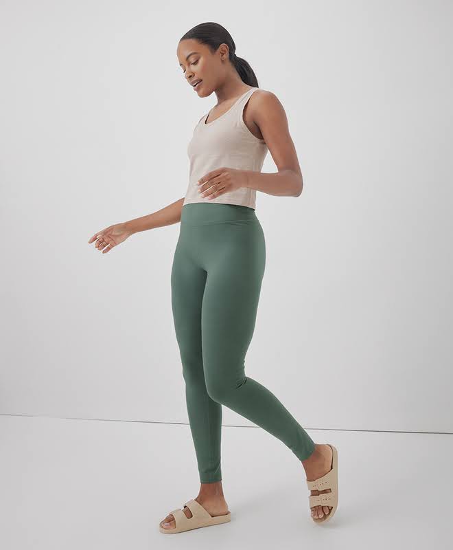 A woman wearing green cotton tights from pact and a beige tank top with beige slides