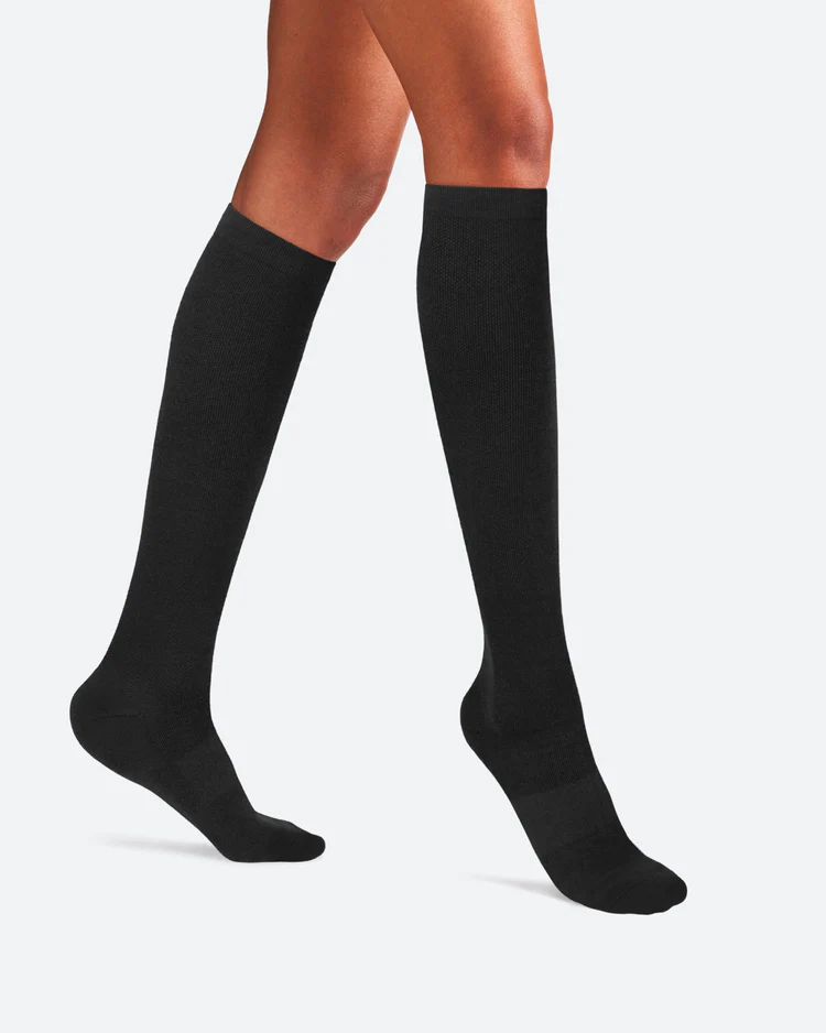 A woman wairing solid black knee-high bamboo compression socks from Ostrichpillow