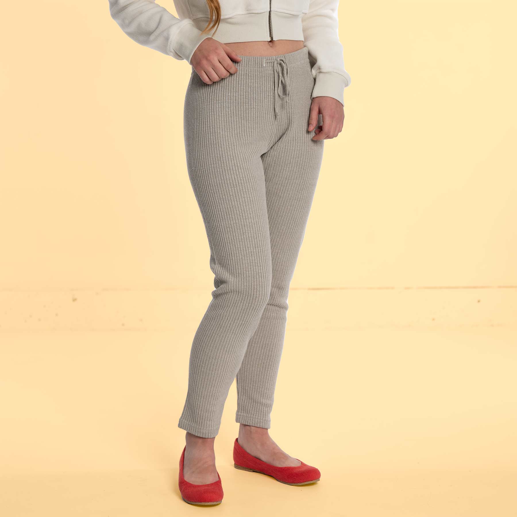 A woman wearing the Santa Barbara linen leggings from Rawganique, a white zip-up, and red flats