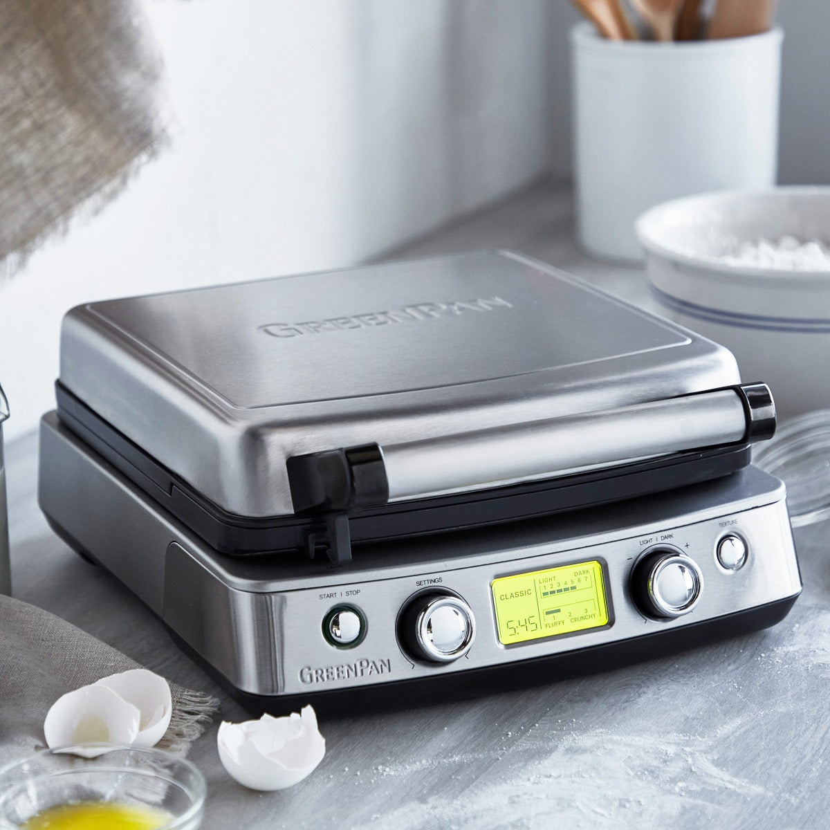 Elite Ceramic Nonstick Waffle Maker from GreenPan placed on a kitchen countertop with eggs and flour nearby