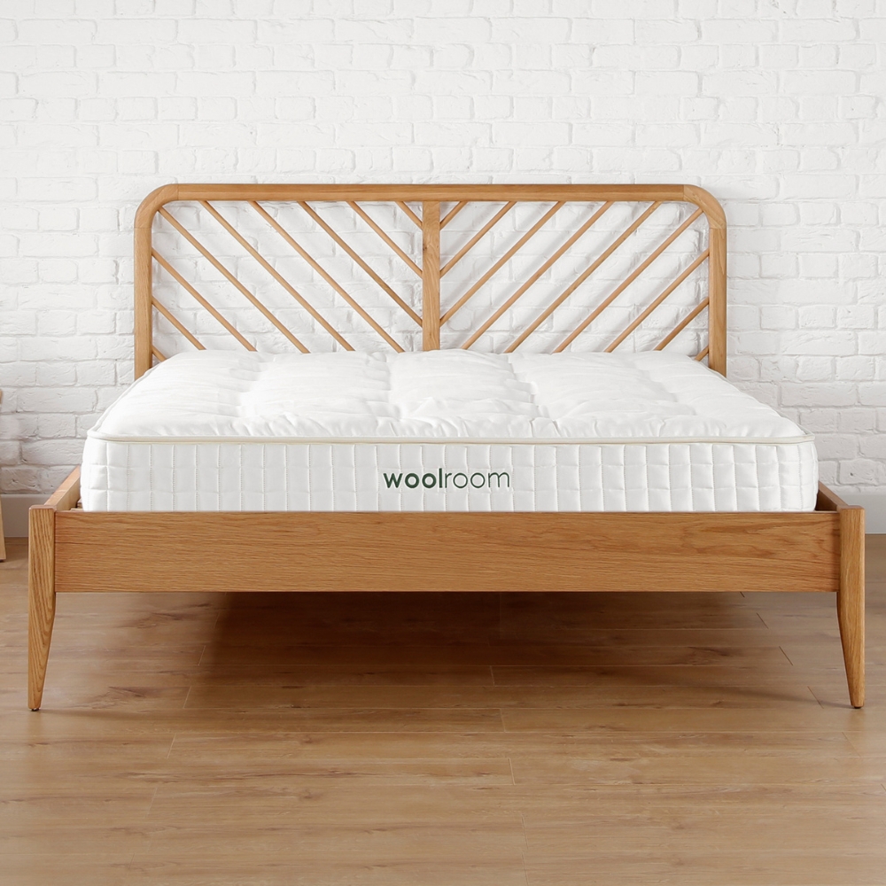 A classic Woolroom wool mattress on a brown wooden bed frame with a slatted headboard