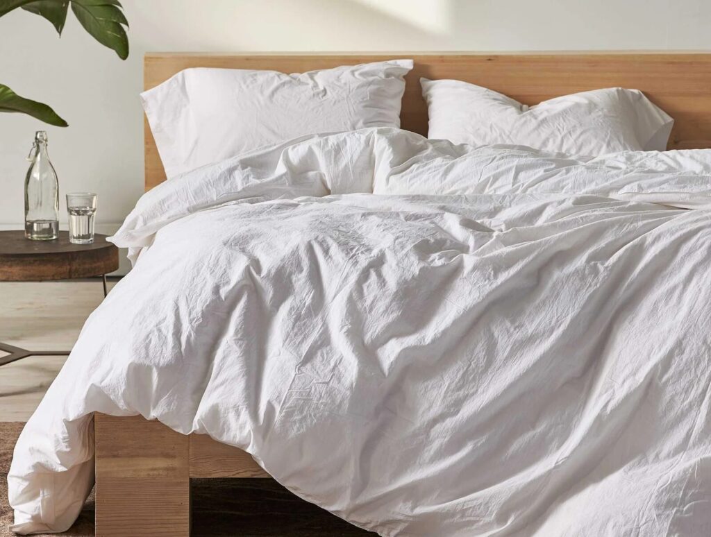 White natural cotton sheets, blankets, and pillowcases on a wooden bed frame