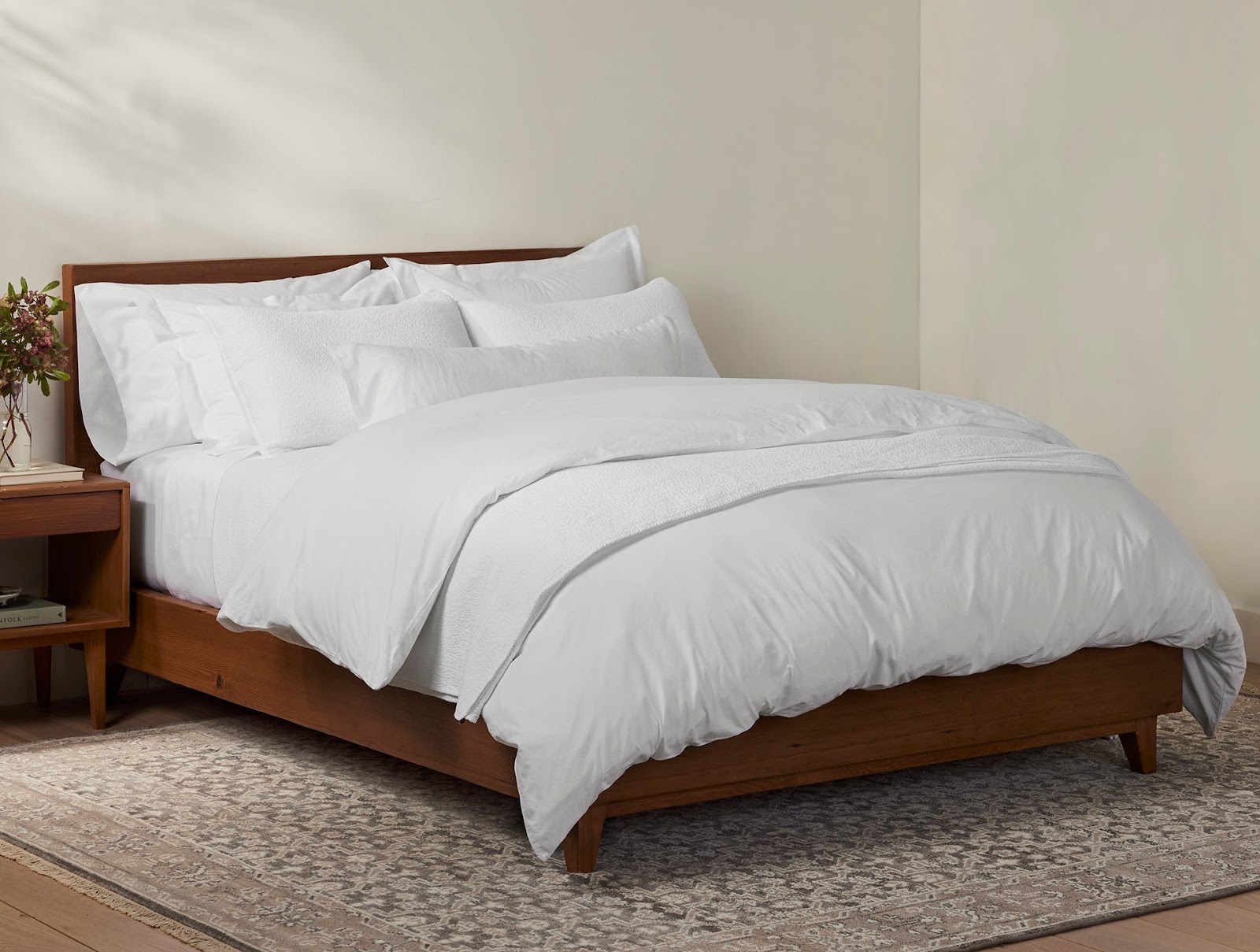 A wooden bed frame with a mattress covered in a white organic percale sheet set from Coyuchi