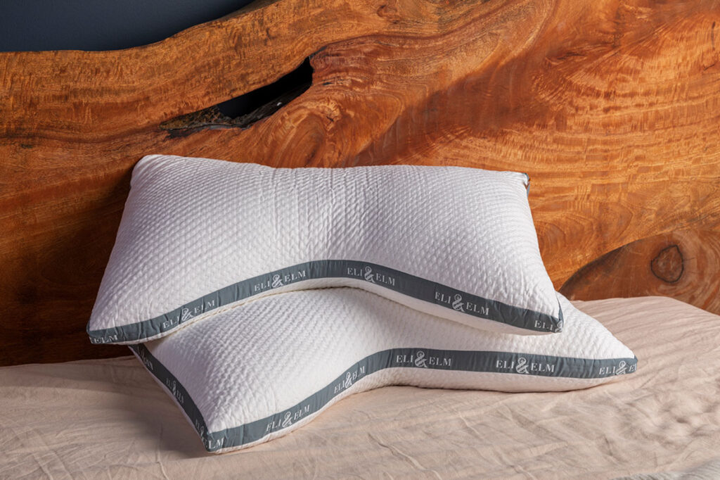 Two Eli & Elm Cooling side sleeper cotton pillows on a bed with a wooden bed frame