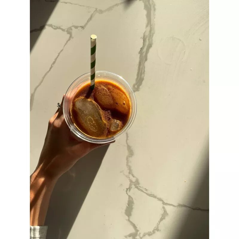 A woman’s hand holds a glass cup with a green and white striped paper straw inside