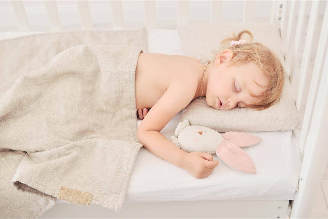 A baby sleeping in a crib covered with a linen weighted blanket