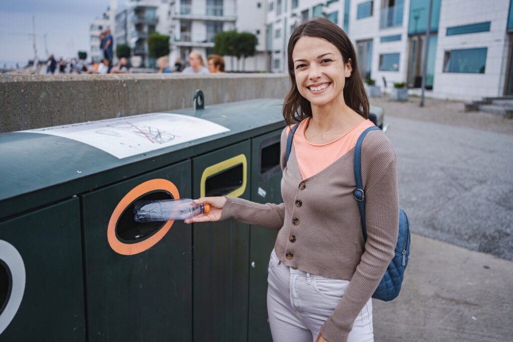 Young woman throwing a plastic bottle in a recycling bin in a malmo street