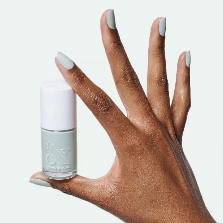 A woman’s hand holding a bottle of mint-colored non-toxic nail polish from Olive & June between her thumb and pointer finger