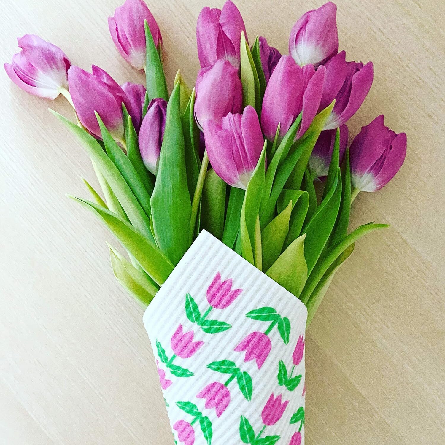 A bouquet of pink tulips wrapped in a Swedish dishcloth with a pink tulip pattern.