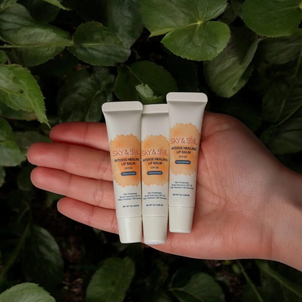 An open hand holding three tubes of Sky & Sol Lip Jelly over a background of green leaves.